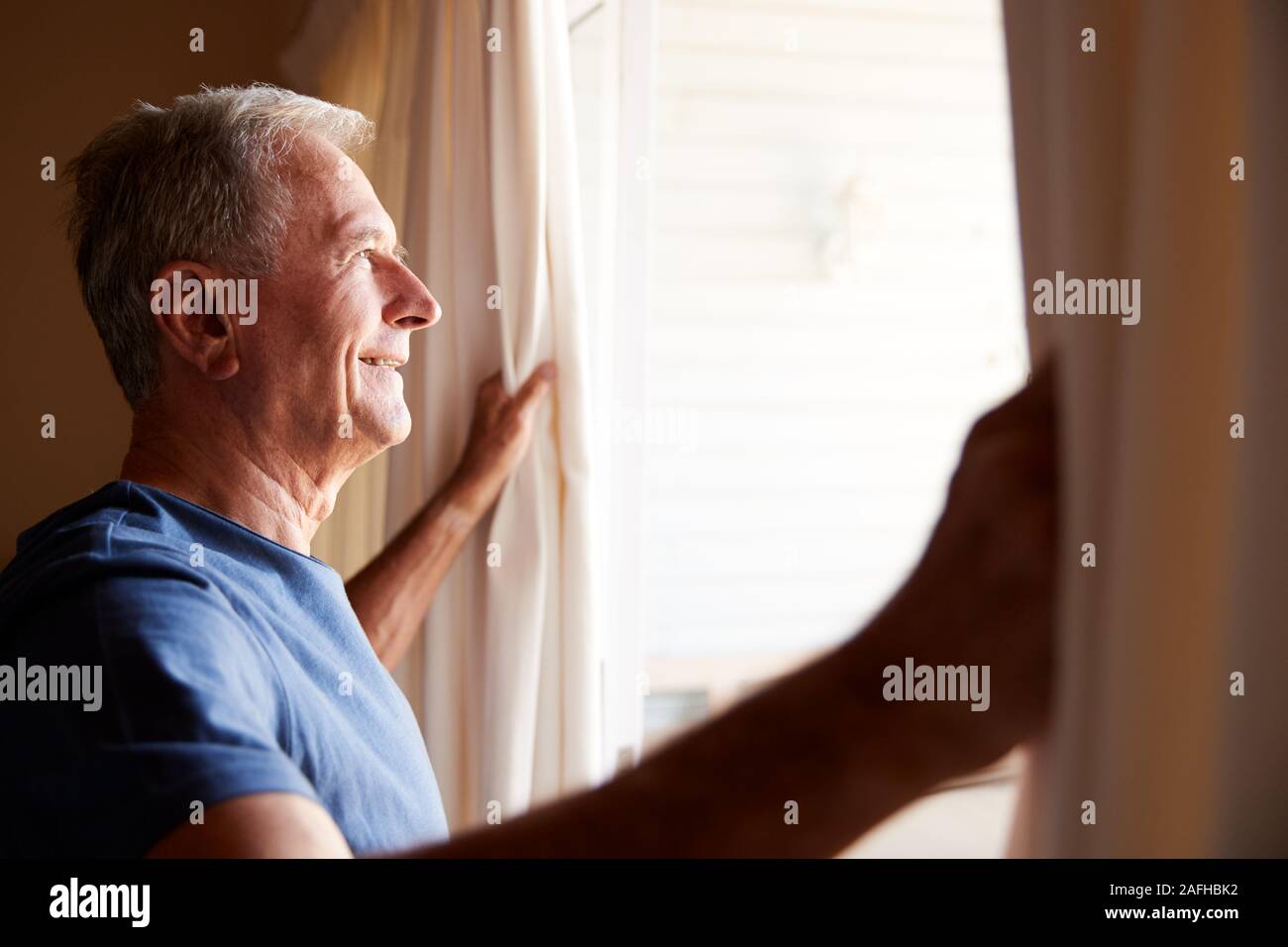 Senior sonriente hombre blanco abrir las cortinas en una mañana soleada, vista lateral, cerrar Foto de stock
