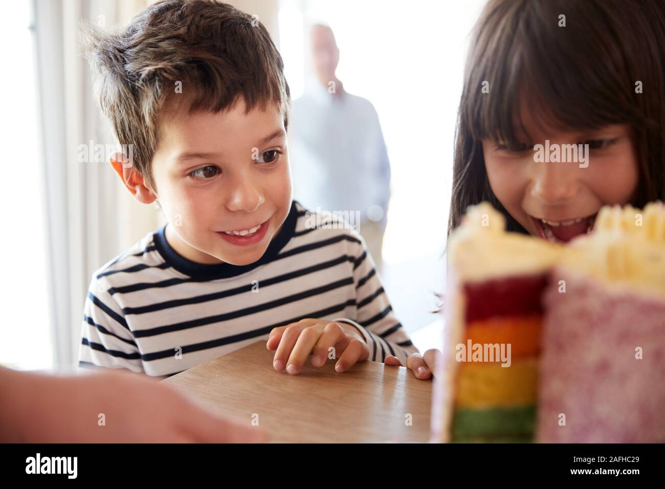 Hermanos jóvenes mirando un colorido pastel de cumpleaños en rodajas sobre una mesa estrecha, el enfoque selectivo Foto de stock