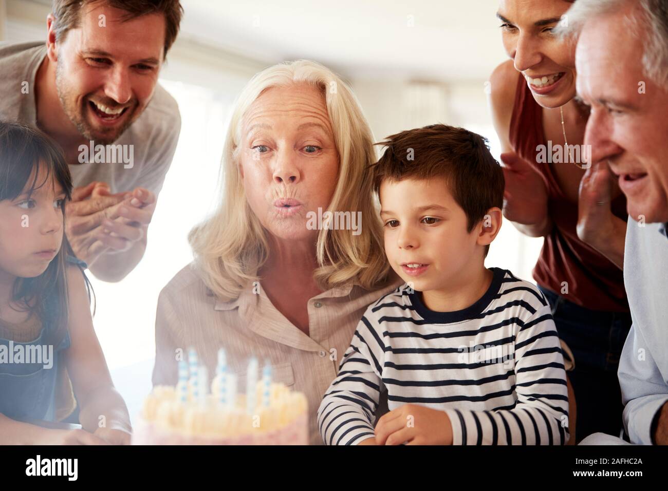 Senior mujer blanca celebra su cumpleaños con la familia soplar las velas de su pastel Foto de stock