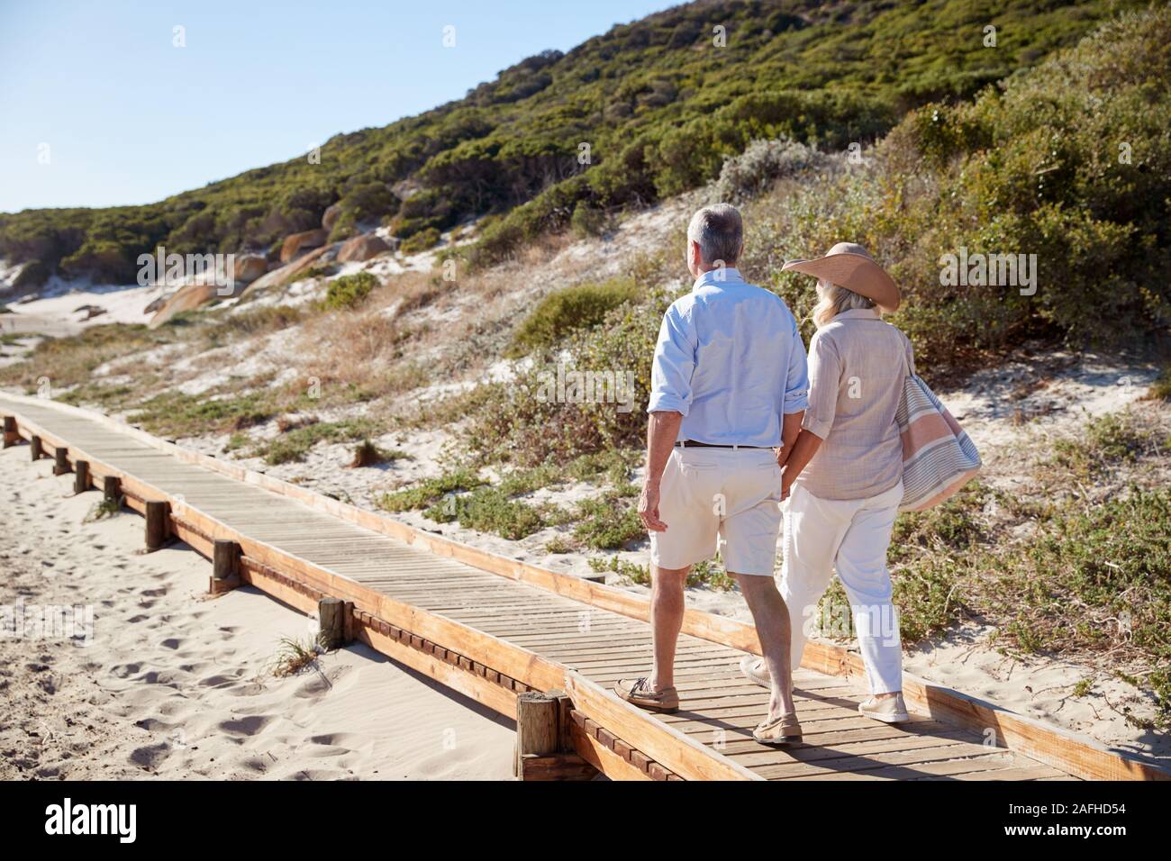 Senior pareja blanca caminando a lo largo de paseo de madera en la playa cogidos de la mano, longitud completa, vista posterior Foto de stock
