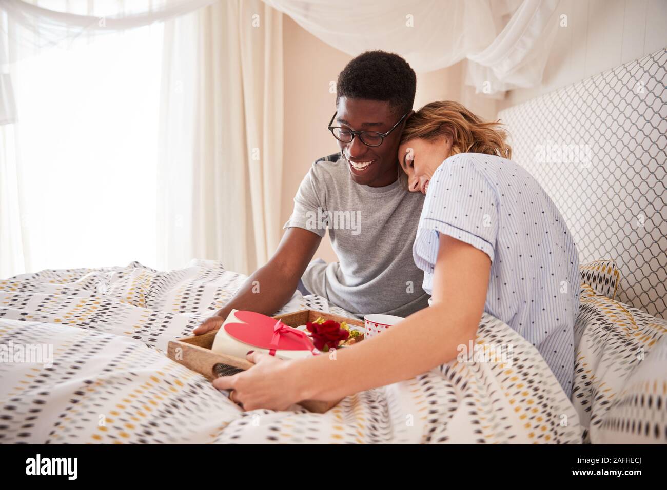 Mestizos pareja abrazada, hombre llevando su partner y regalos desayuno en la cama, cerrar Foto de stock