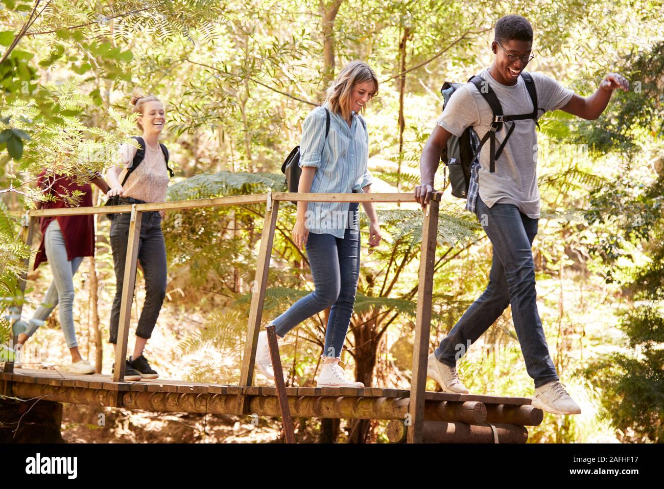 Adultos jóvenes amigos cruzando un puente peatonal durante una caminata en el bosque, longitud completa Foto de stock