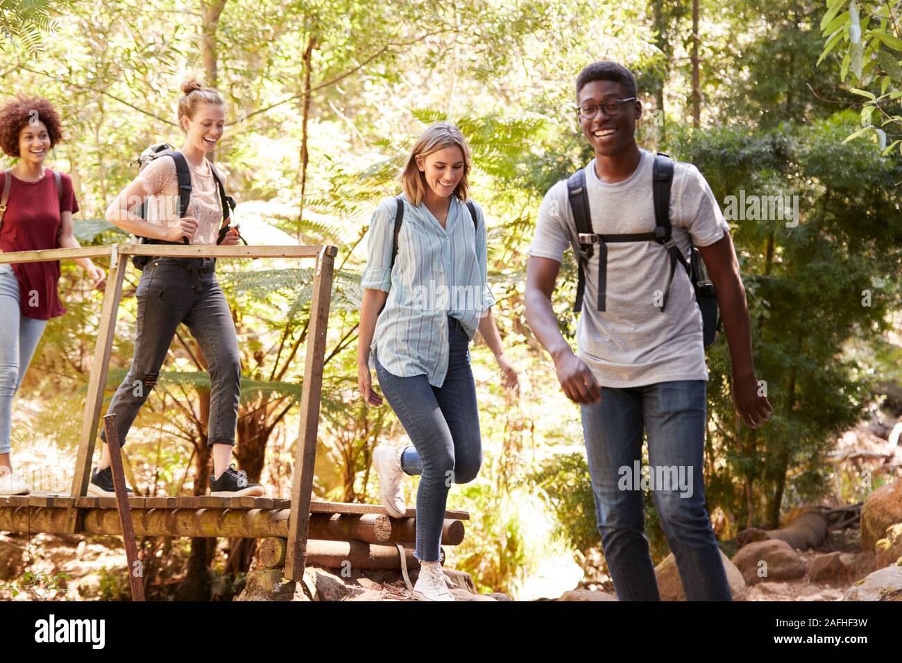 Adultos jóvenes amigos cruzando un puente peatonal durante una caminata en el bosque, longitud completa Foto de stock