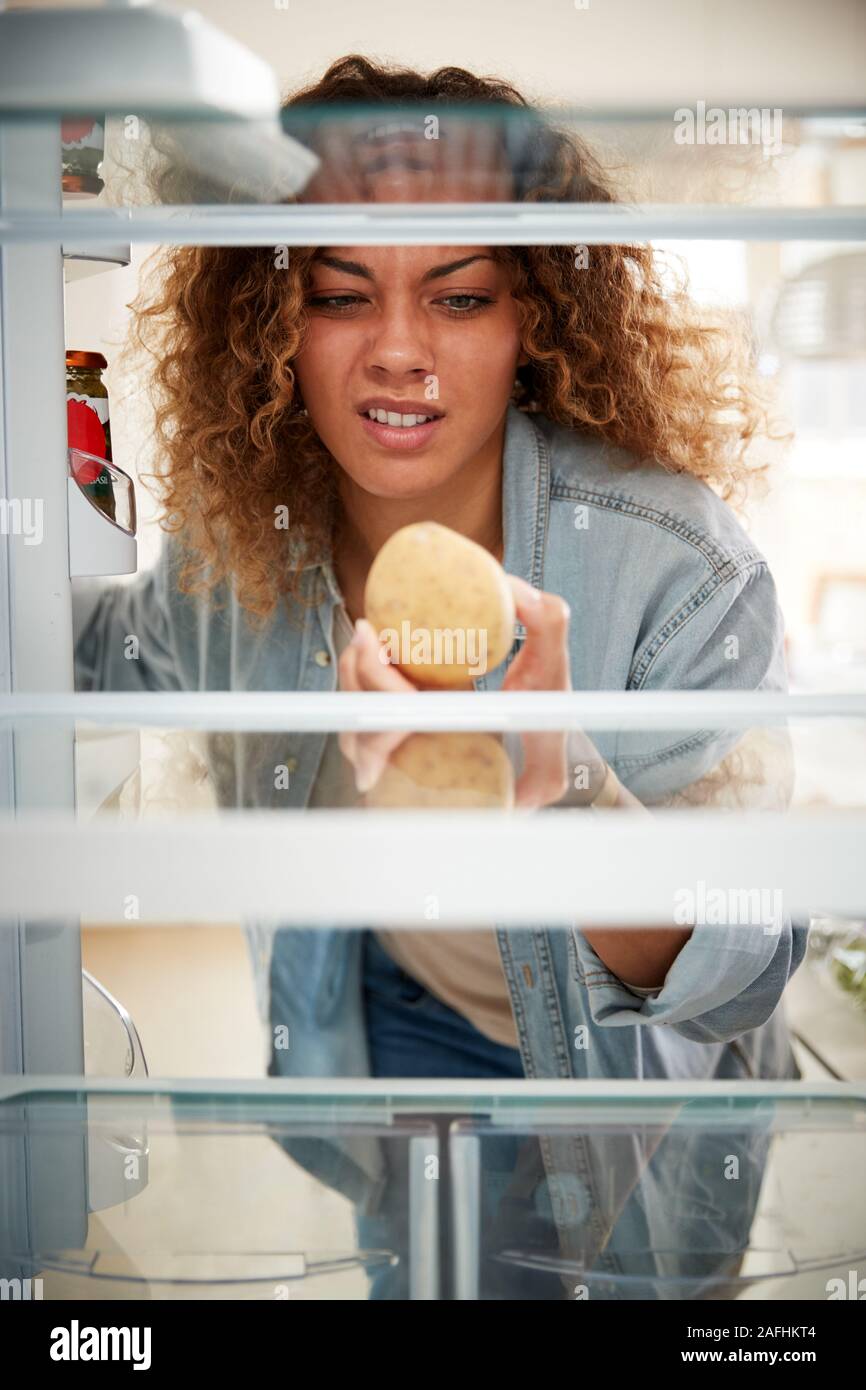 Decepcionado mujer mirando dentro del refrigerador vacío, excepto para la patata en la estantería Foto de stock