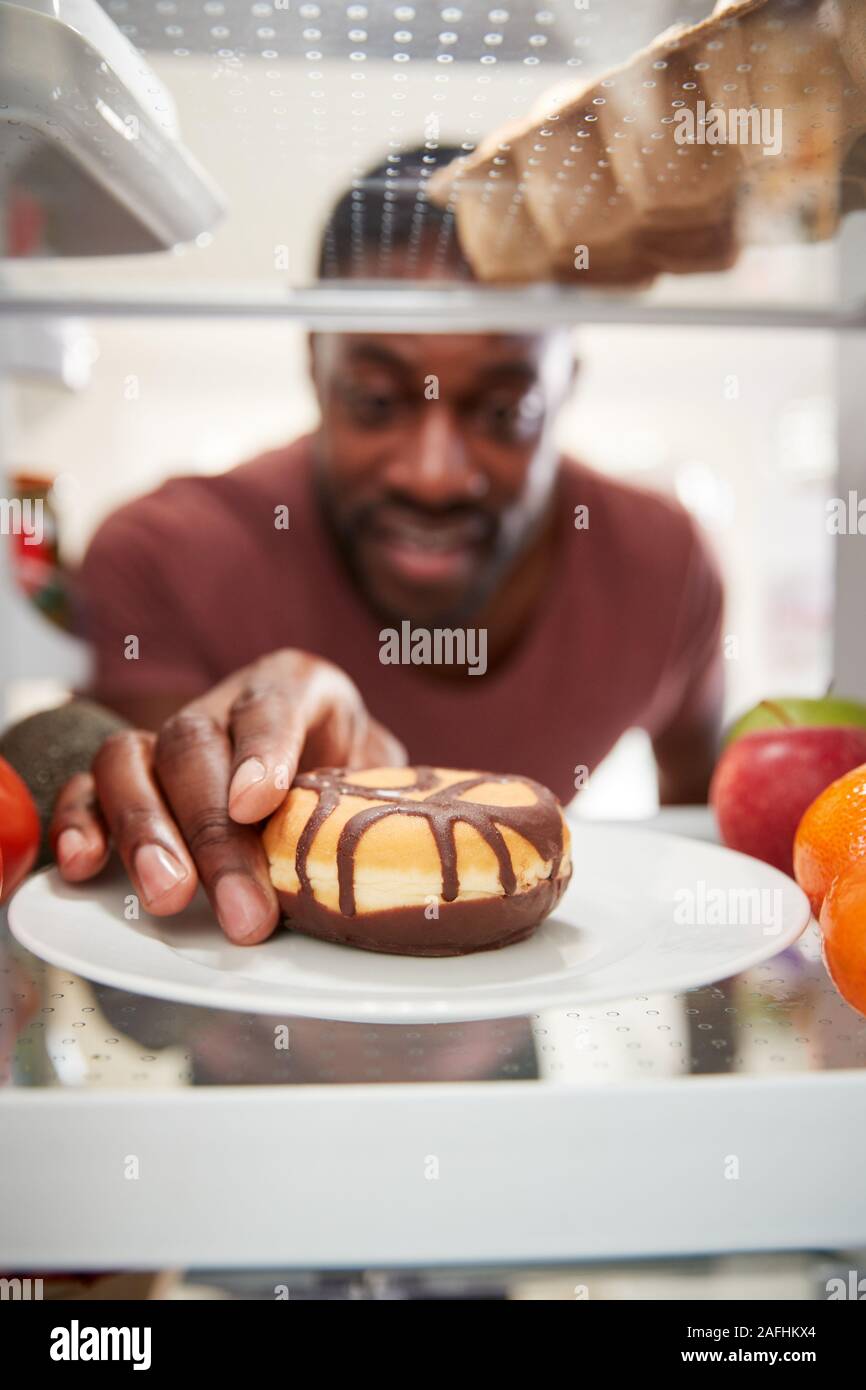 Vista desde el interior de la nevera como hombre abre la puerta y alcanza para insalubres Donut Foto de stock
