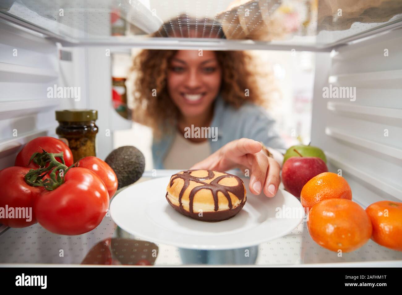 Vista desde el interior de la nevera como la mujer abre la puerta y alcanza para insalubres Donut Foto de stock
