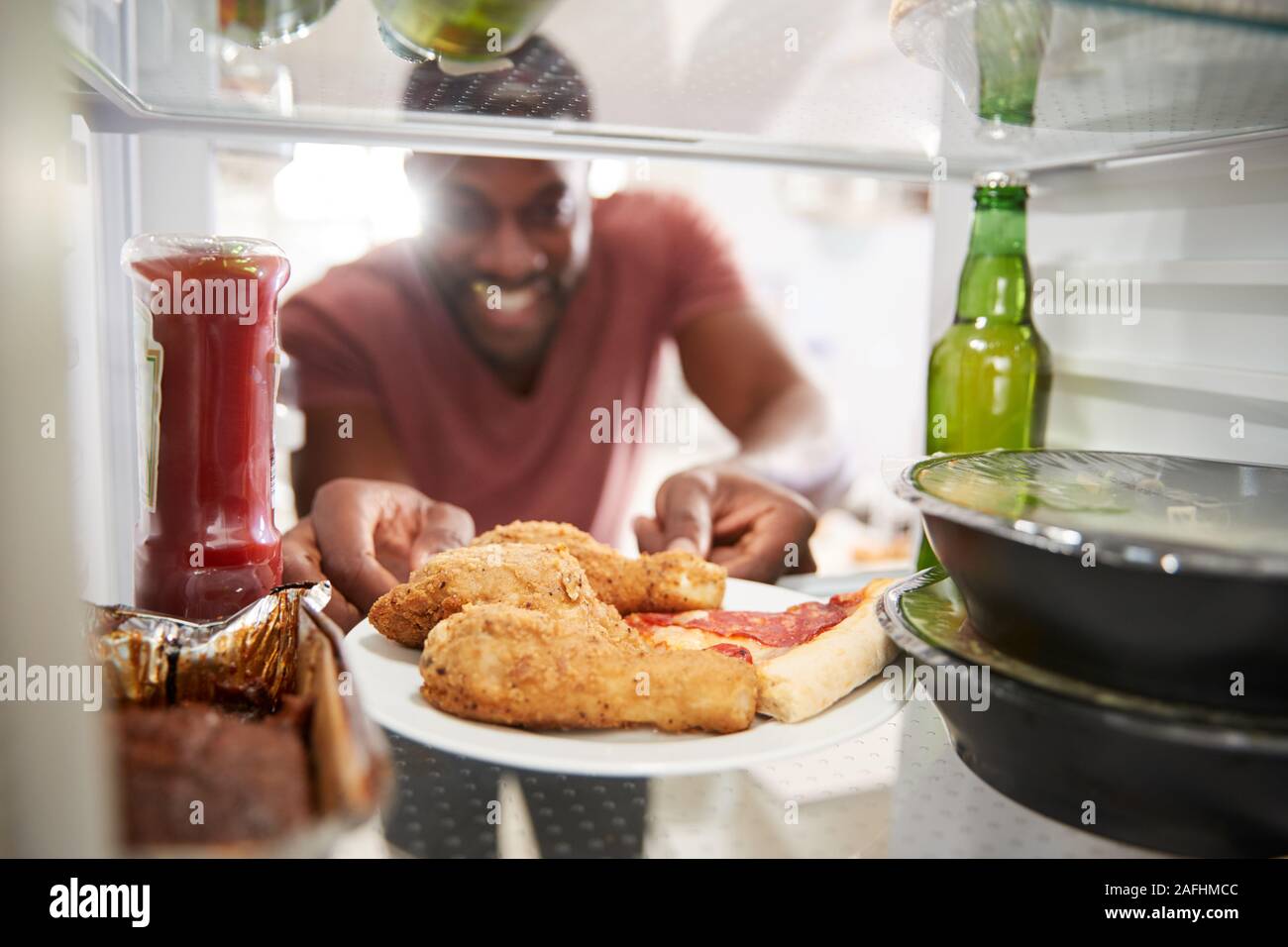 Vista desde el interior de la nevera llena con comida para llevar, insalubre hombre abre la puerta Foto de stock
