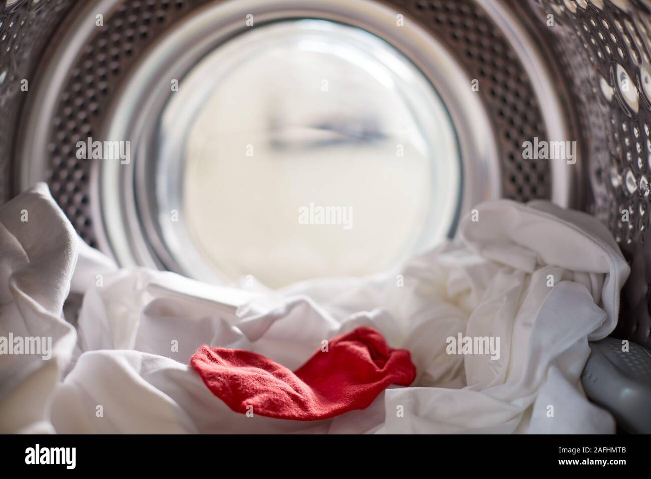 Vista desde el interior de la lavadora con calcetines rojos mezclados con ropa blanca Foto de stock