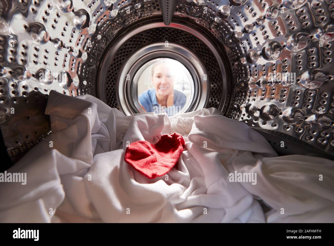 Mujer mirando dentro de la lavadora con calcetines rojos mezclados con ropa blanca Foto de stock