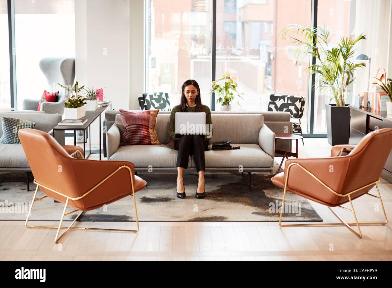 La empresaria sentada en un sofá con un portátil en una mesa de trabajo en la oficina del área de trabajo compartida Foto de stock