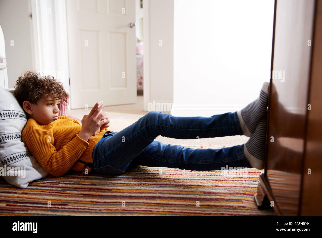 Niño acostado en el piso del dormitorio dedica demasiado tiempo a través de teléfono móvil Foto de stock