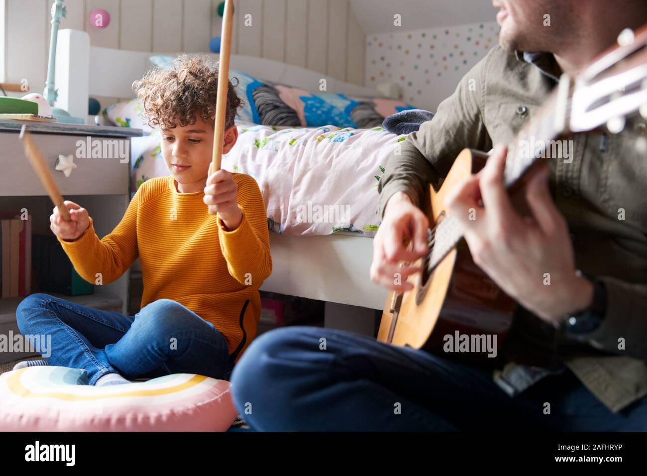 Solo padre tocando la guitarra con el Hijo que los tambores en el cojín en dormitorio Foto de stock