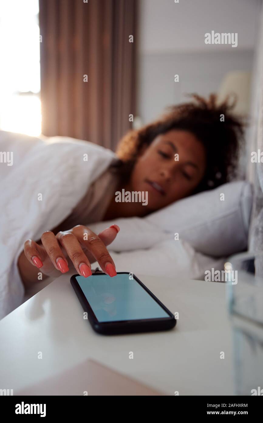 Mujer de despertarse en la cama llega a desactivar la alarma en el teléfono móvil Foto de stock