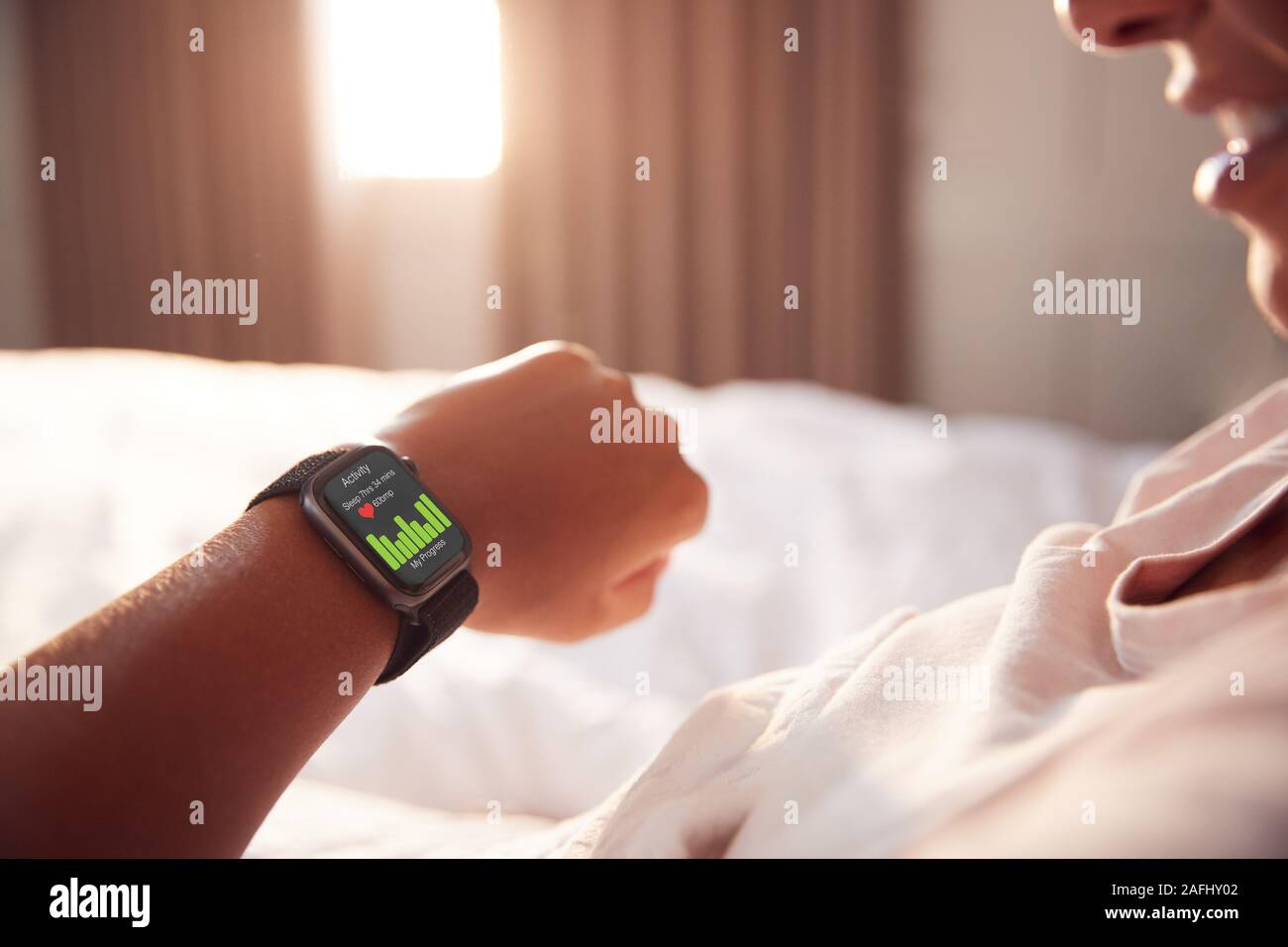 Mujer sentada en la cama mirando la pantalla de reloj inteligente Foto de stock