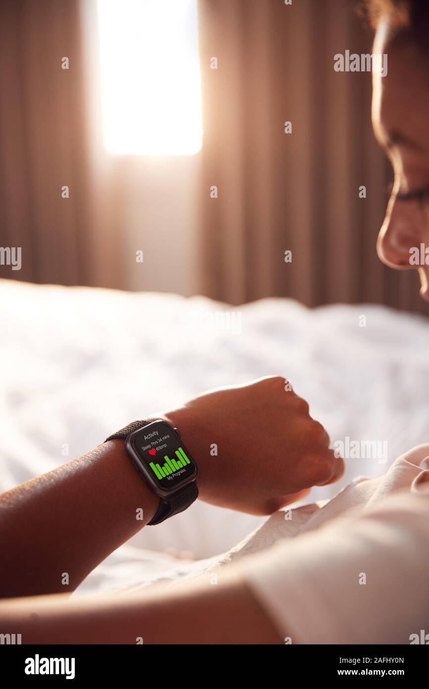 Mujer sentada en la cama mirando la pantalla de reloj inteligente Foto de stock