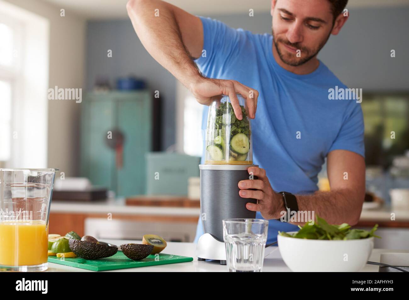 Hombre haciendo jugos saludables con ingredientes frescos en la licuadora eléctrica después del ejercicio Foto de stock
