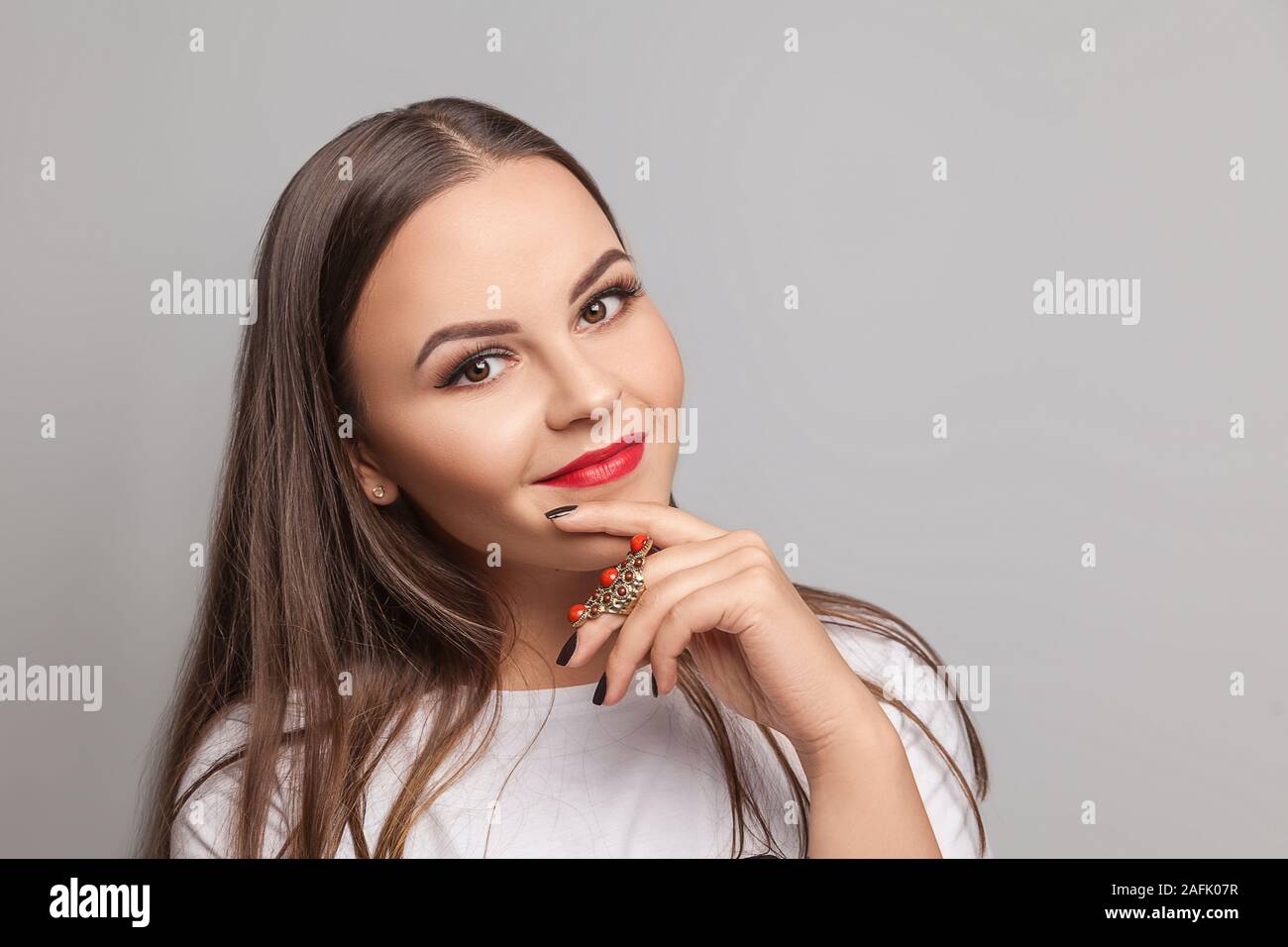 Retrato de joven morena juguetona sexy chica vestida de blanco camiseta permanente aisladas contra un fondo gris. Mujer mirando a la cámara. Foto de stock