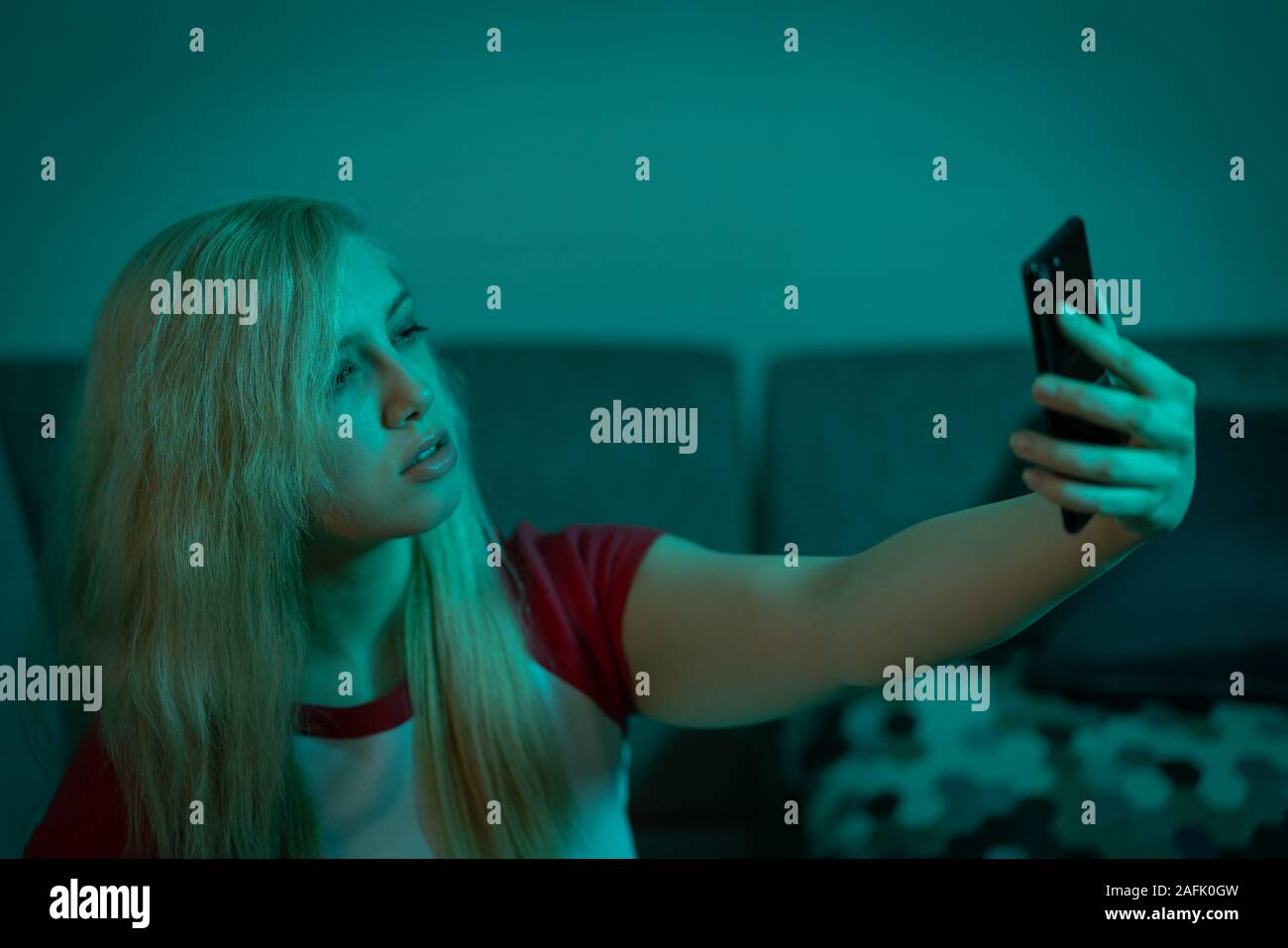 Jóvenes aburridos chica teniendo selfie milenario en verde azulado iluminación con teléfono móvil Foto de stock
