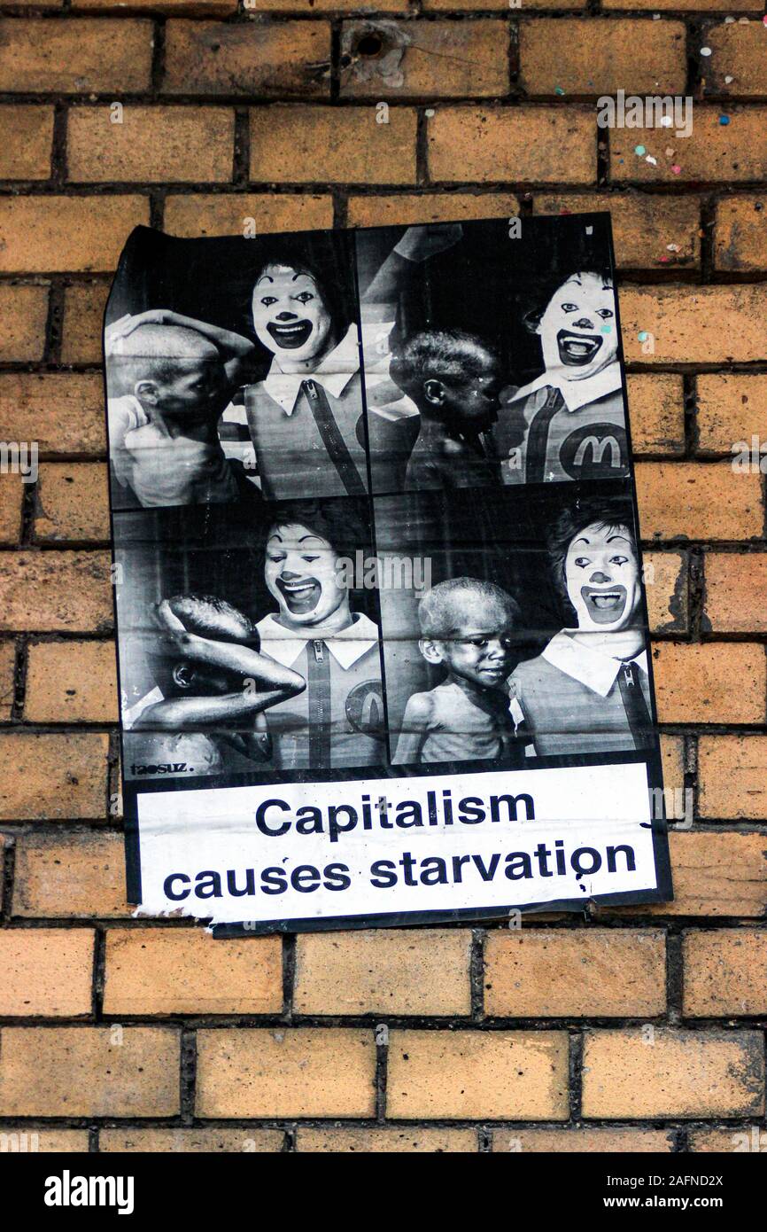 El capitalismo produce hambre - wheatpaste cartel sobre pared de ladrillo amarillo en Berlín, Alemania Foto de stock