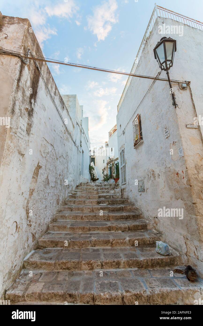 Pasadizo y pasos en un tramo de escaleras en un callejón en el centro histórico casco antiguo de Ostuni, Brindisi, Apulia, en el sur de Italia, en la luz del atardecer Foto de stock