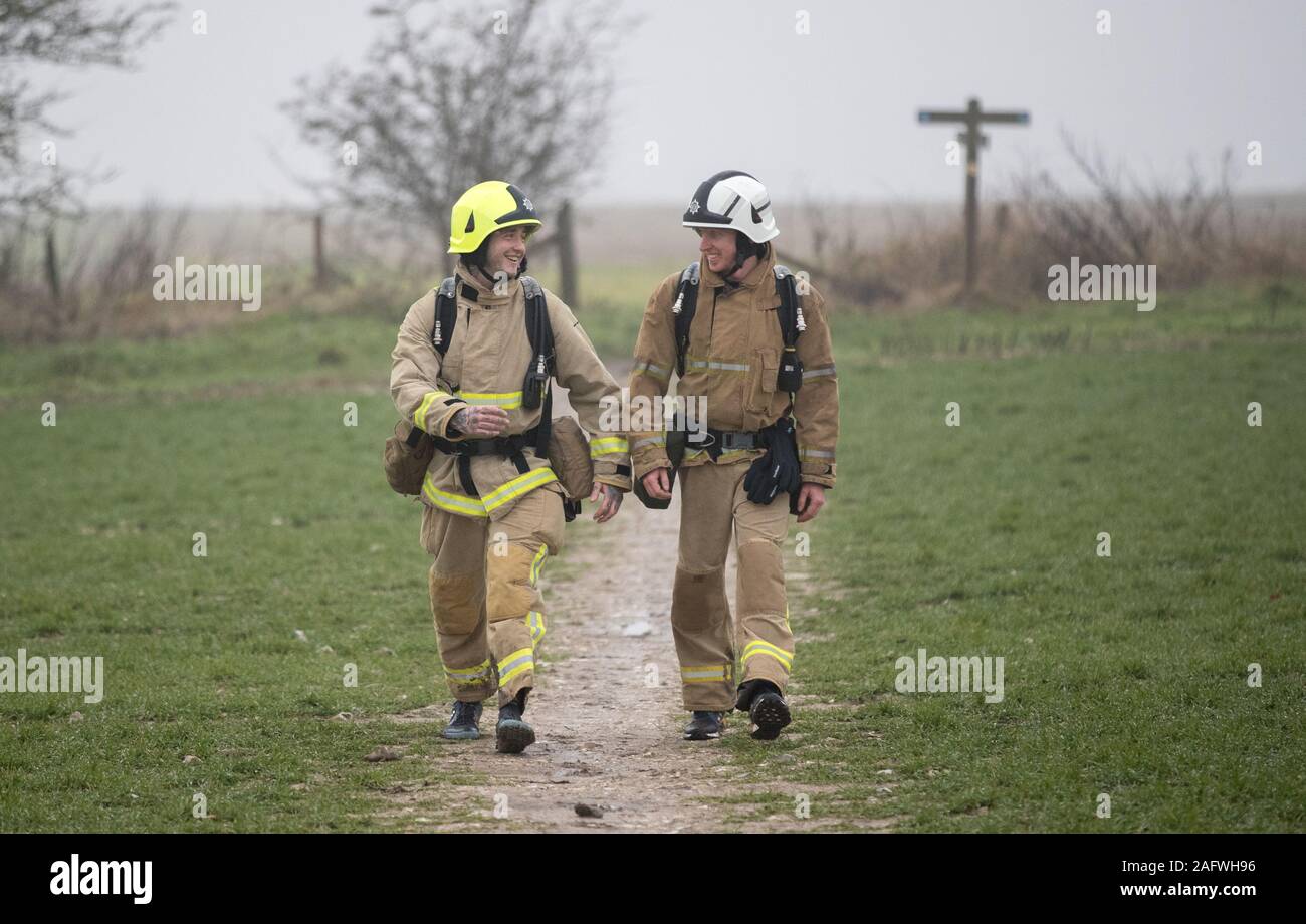 Los bomberos Shaun Challis (derecha) y Lee Smith de West Sussex Servicio de Incendios y rescate, caminar a lo largo de los South Downs camino cerca de Winchester Hampshire, como ellos salieron en una caminata benéfica en Eastbourne, vistiendo completo kit de fuego, recaudar dinero para Martlets Hospicio y los Bomberos de la caridad. Foto de stock