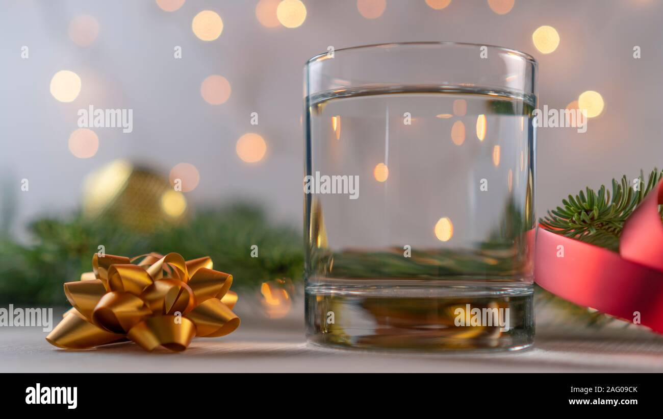 Un vaso con una gruesa abajo llena con un líquido claro con adornos de  Navidad y ramas frescas de un árbol de Año Nuevo y una hermosa cinta roja.  Ag Fotografía de