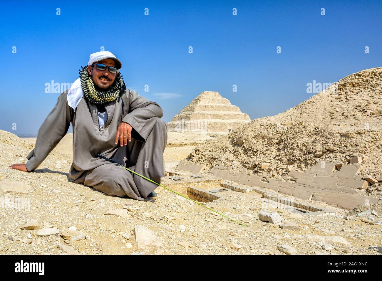 Guía de camellos sentados en las dunas de arena junto a la Pirámide de Anus con el paso pirámide en el fondo Foto de stock