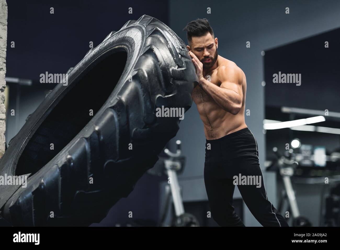 Tío musculoso descamisados flipping enorme neumático de gimnasio Fotografía  de stock - Alamy