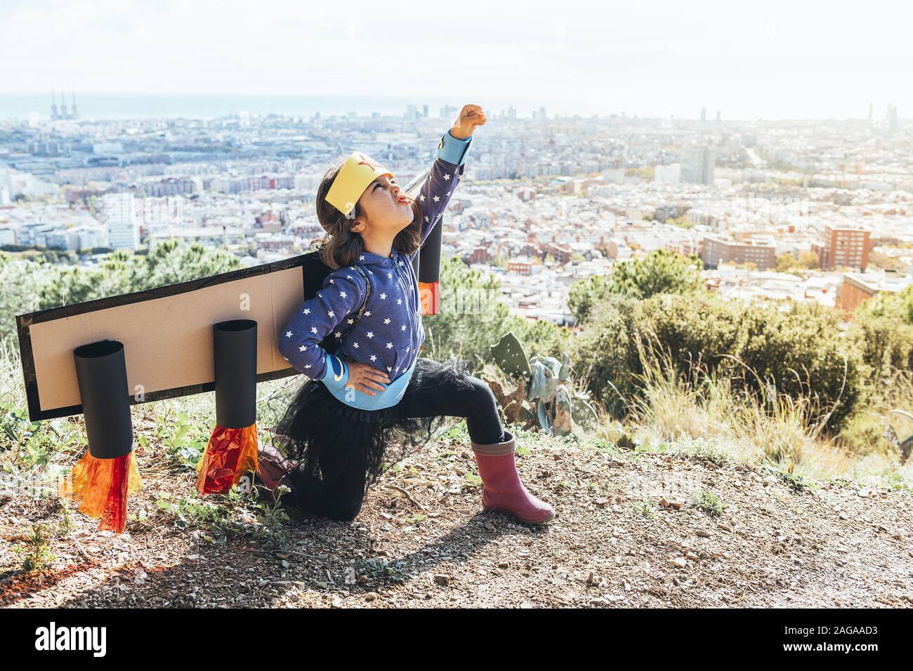 Gracioso niño niña plantea potente disfrazada como un superhéroe con traje  casero y alas de avión de cartón delante de un paisaje urbano, la  imaginación de un Fotografía de stock - Alamy