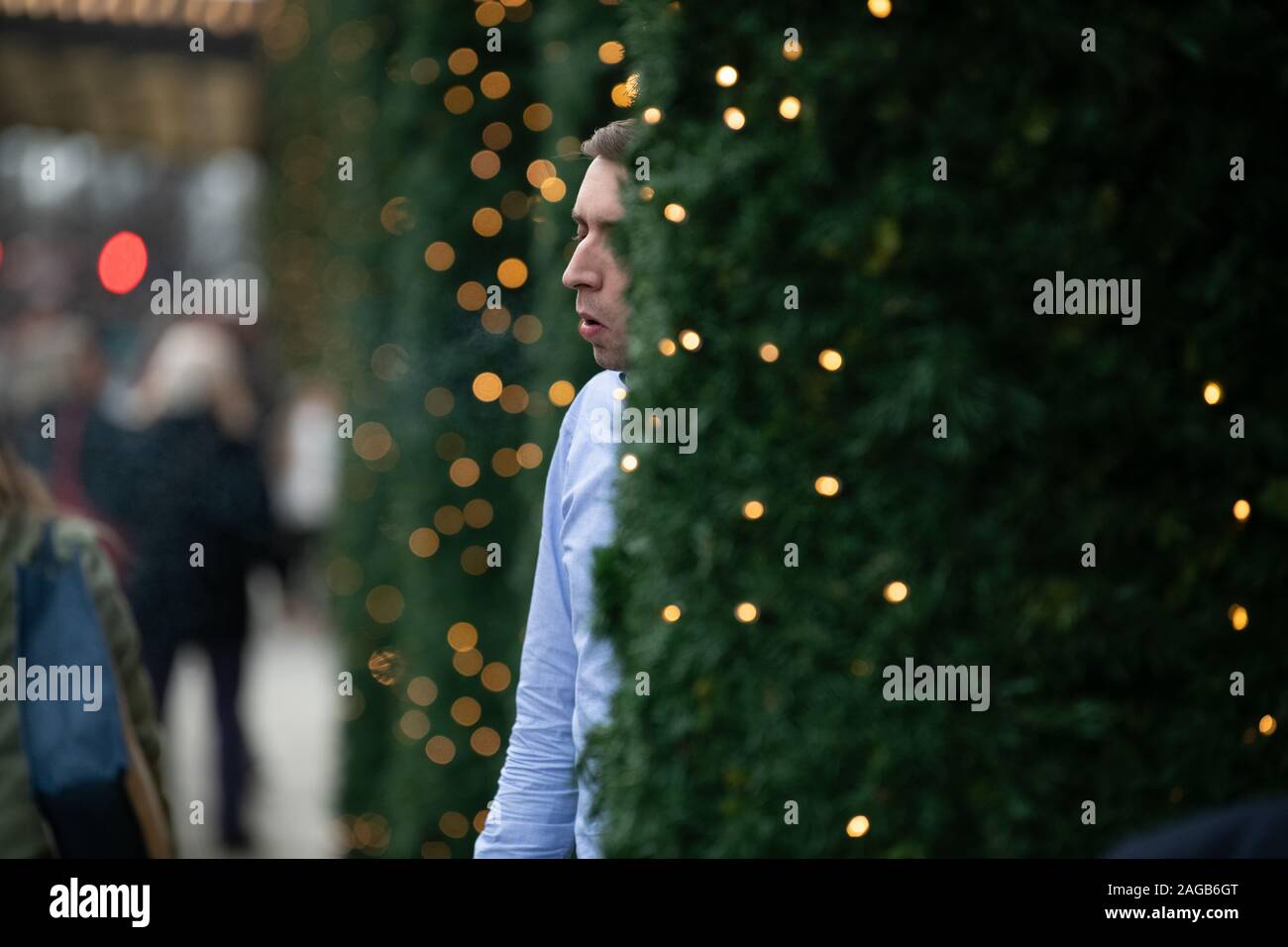 El hombre fumar un cigarrillo entre los árboles de Navidad fuera de Selfridges en la Oxford Street, las luces de Navidad en vista Foto de stock