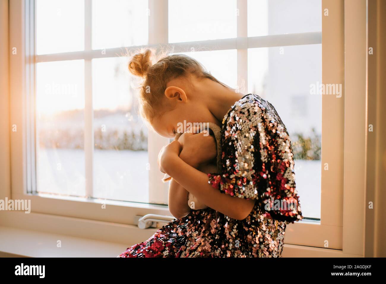Niña jugando con su juguete en casa en un brillante vestido al atardecer Foto de stock
