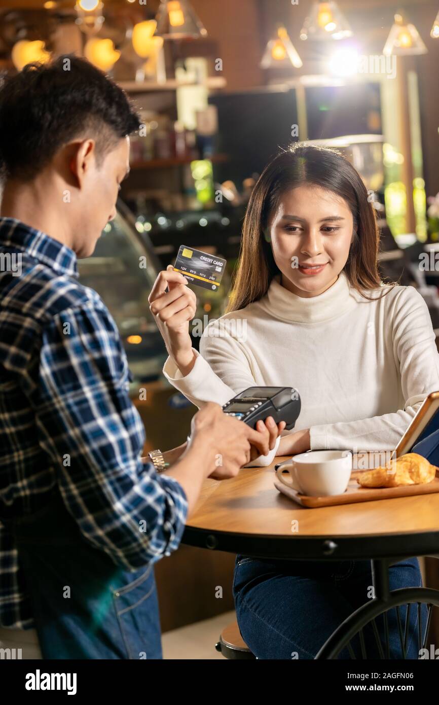 Clientes asiáticos usando tarjeta de crédito sin contacto con tecnología nfs para pagar un camarero para compra de café en la mesa de café. Foto de stock