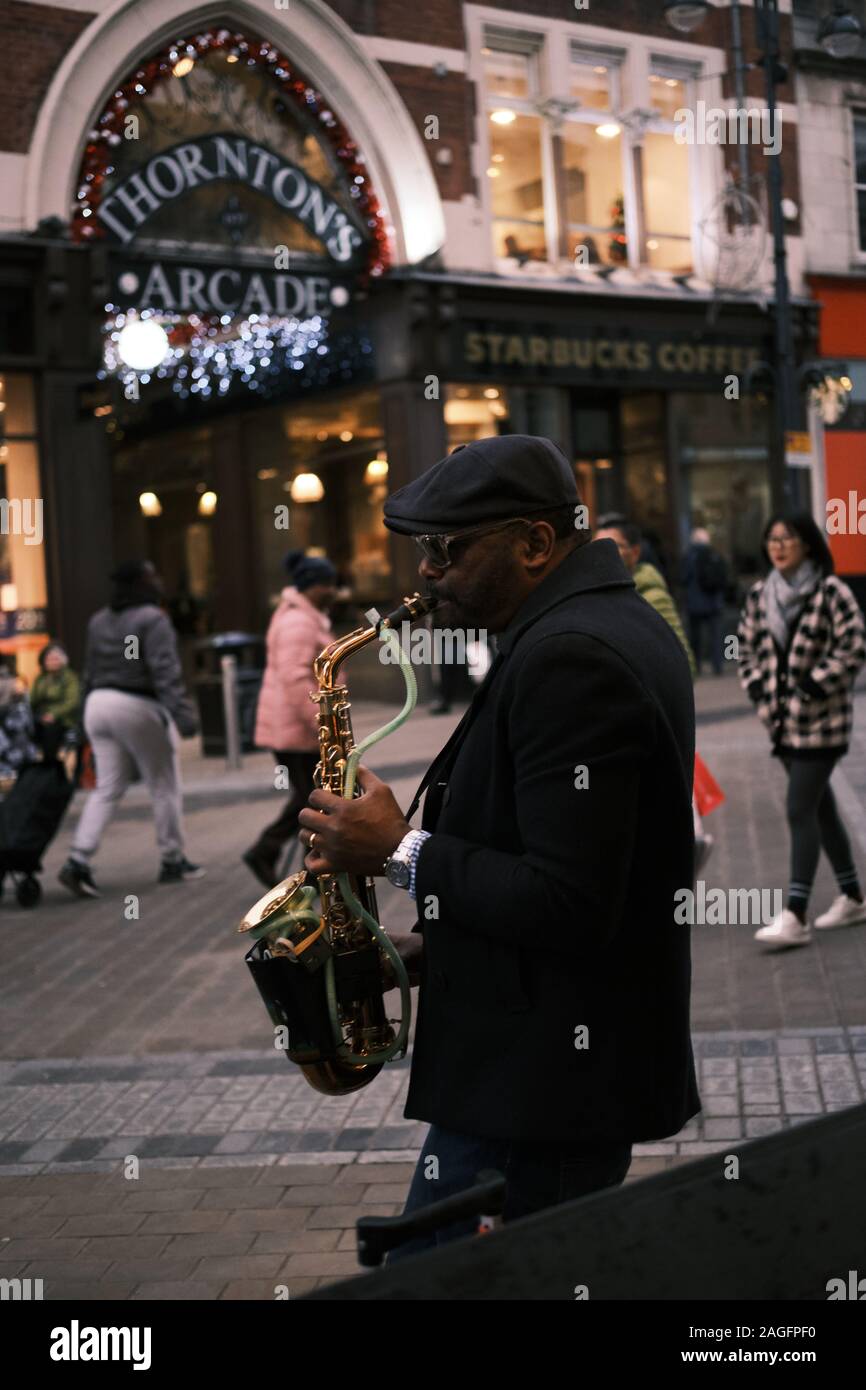LEEDS, REINO UNIDO - Dec 07, 2019: un músico callejero tocando su saxofón en Leeds Briggate High Street durante un ajetreado día de Navidad Foto de stock