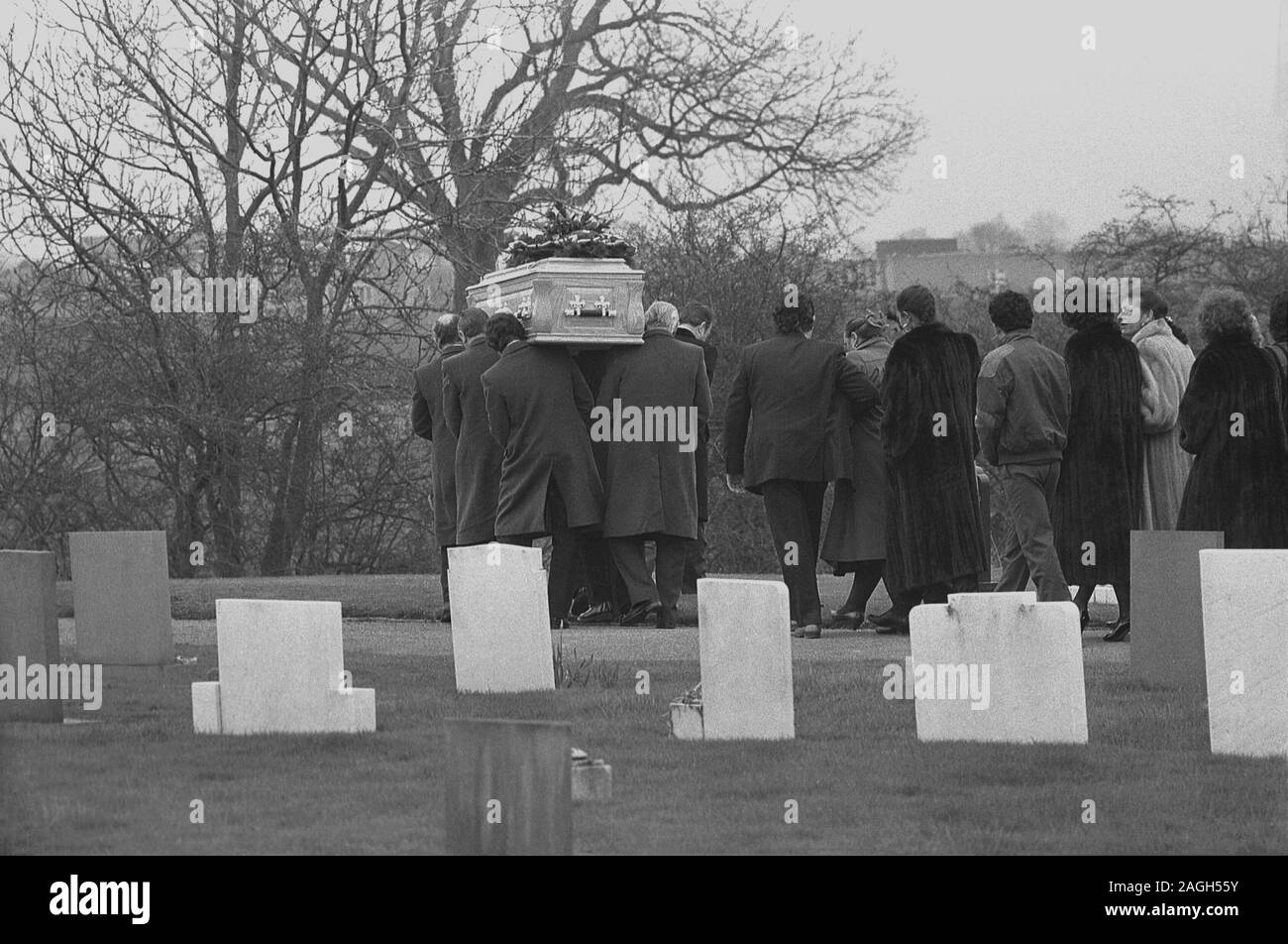 1980, histórico, la gente que asiste a un funeral, con las mujeres usando gruesos abrigos de piel, mientras siguen a los hombres pallbearers que llevan el ataúd sobre sus hombros, a través del cementerio, Inglaterra, Reino Unido, Foto de stock