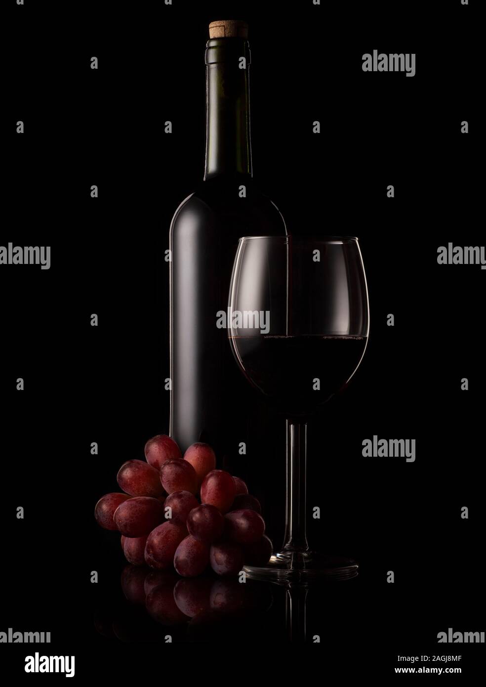 Botella de vino rojo y cristal con fondo negro e iluminación de RIM. Foto de stock