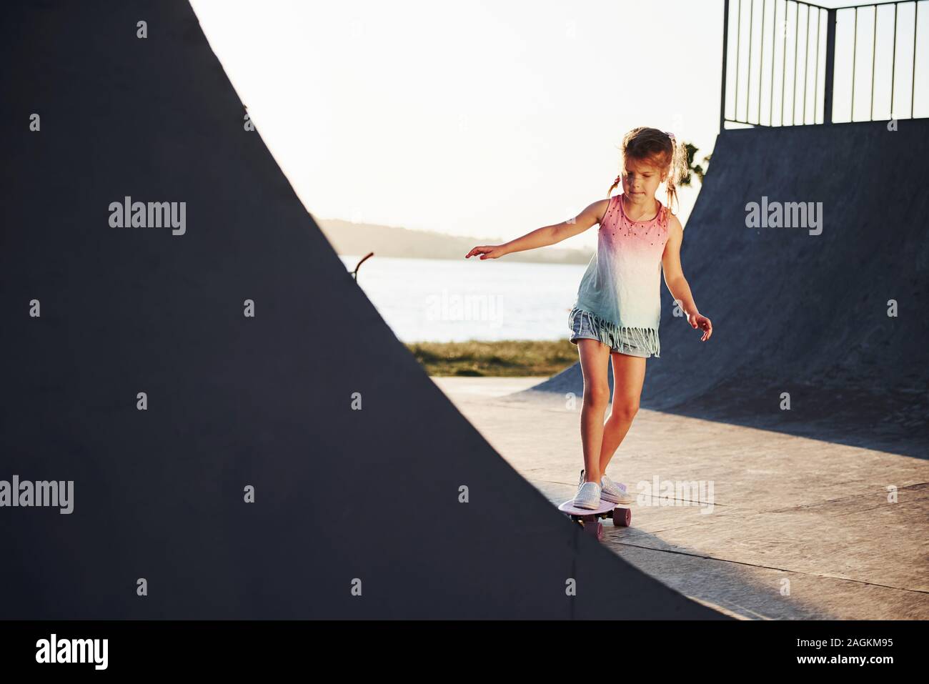 Día soleado. Kid divertirse con el skate en la rampa. Alegre niña Foto de stock