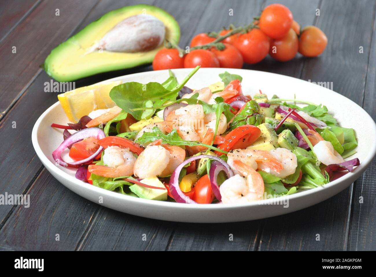 Ensalada de aguacate con gambas, tomates cherry, hojas de remolacha arúgula, cebolla roja, pimiento amarillo dulce. Plato sano con verduras y gambas Foto de stock