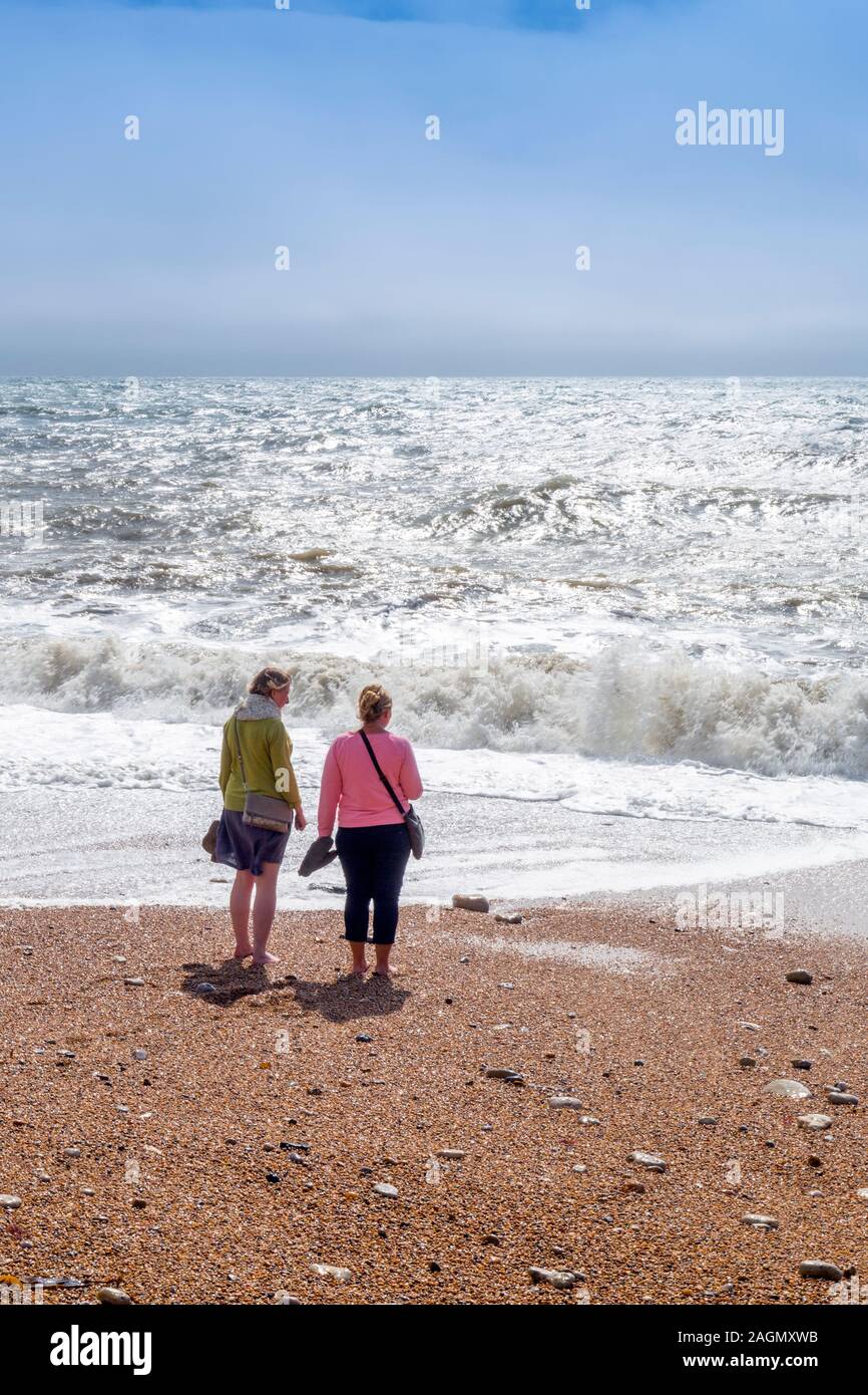 Dos señoras descalzos en la playa en Burton Bradstock sobre la Costa Jurásica como tormenta de otoño olas que rompen sobre la plaqueta, Dorset, Inglaterra, Reino Unido. Foto de stock