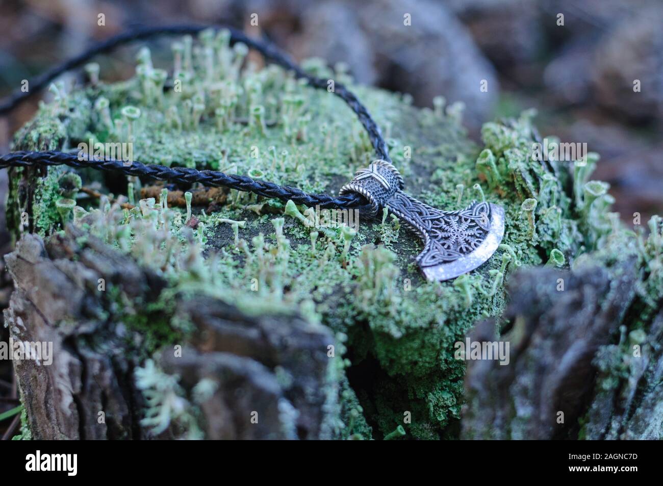 Un martillo de Thor amuleto de plata sobre un tocón cubiertas de musgo Foto de stock