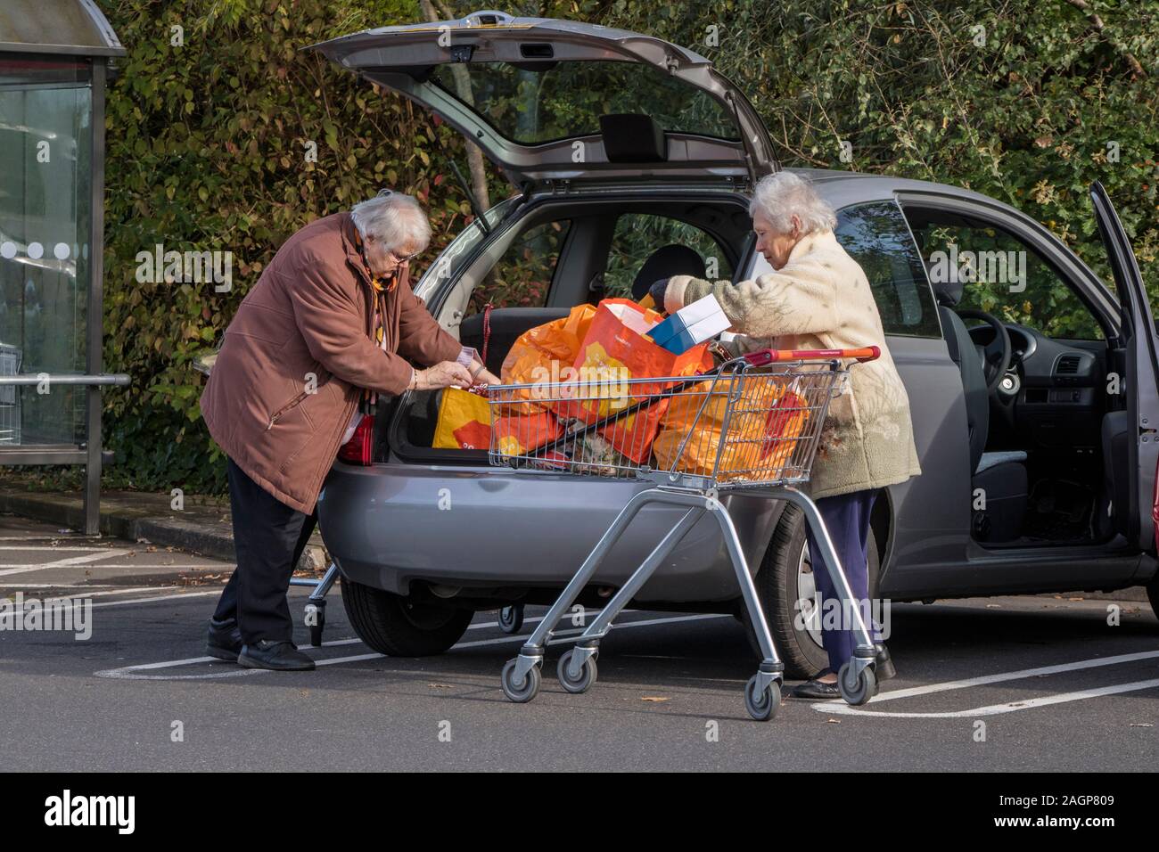 Mujeres mayores descargando compras en su coche en un aparcamiento de supermercado, Inglaterra, Reino Unido Foto de stock