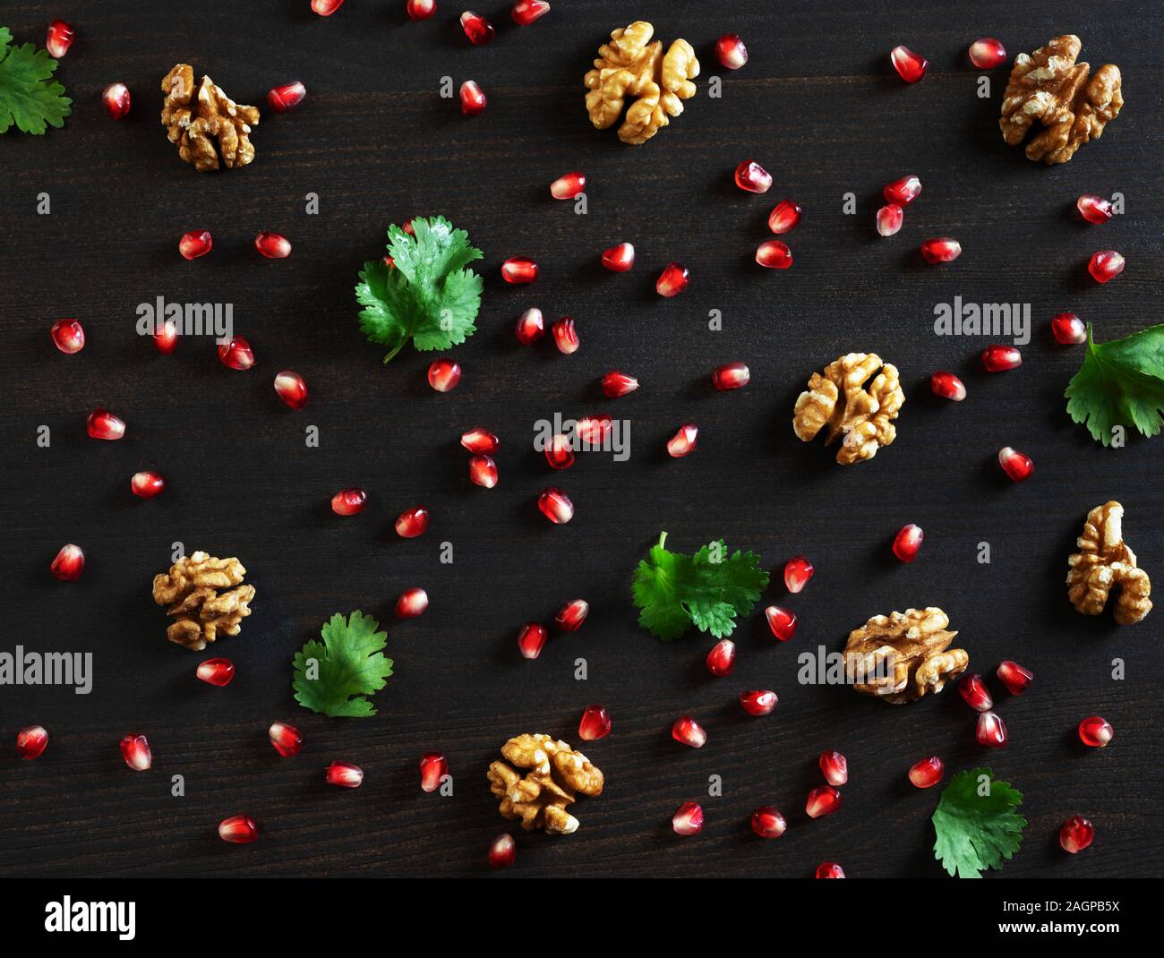 Fondo de alimentos. Semillas de Granada, nueces y cilantro sobre un fondo de madera oscura. Patrón alimentario. Sentar planas, vista superior. Foto de stock