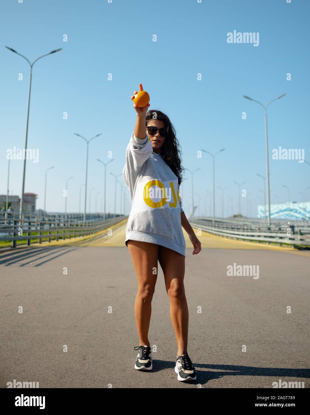 una chica en una sudadera con capucha deportiva lanza una naranja como un béisbol. deporte, fitness Foto de stock