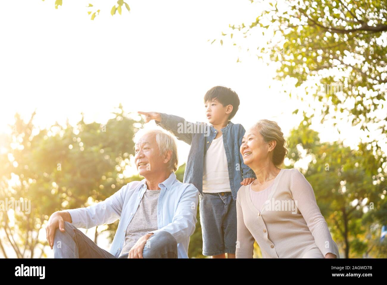 Asia, abuelo y nieto de abuela sentada charlando sobre el césped al aire libre en el parque al atardecer Foto de stock