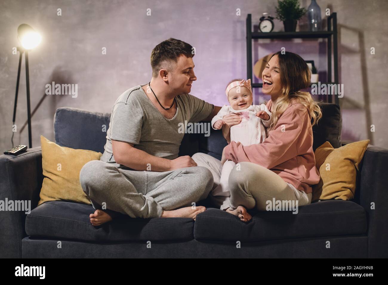 Familia joven sentado en el sofá en una acogedora sala. Mamá, papá y el  bebé están felices Fotografía de stock - Alamy