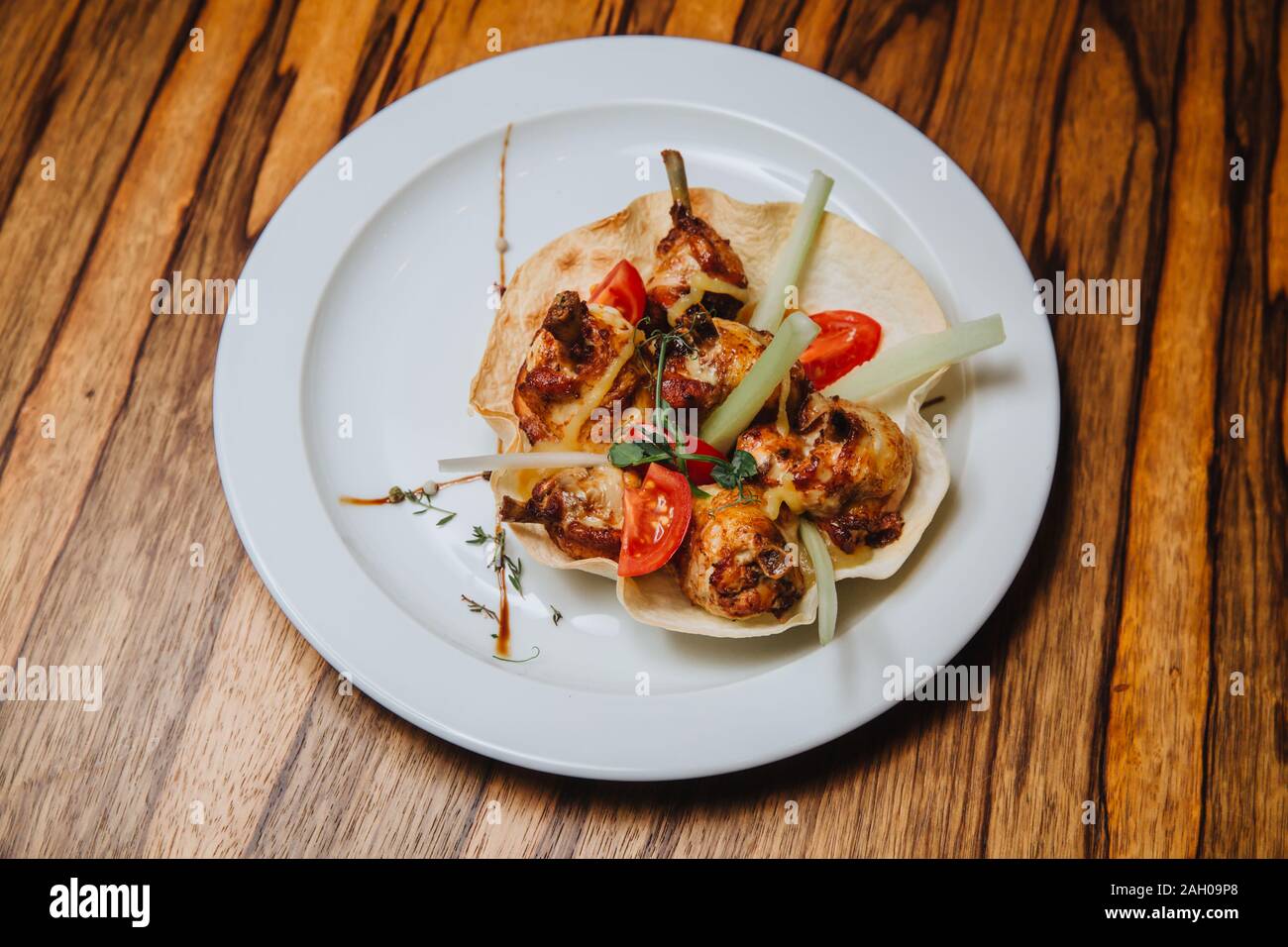 Las alas en salsa de mostaza miel sobre una crujiente tortilla con verduras y hierbas. Foto de stock