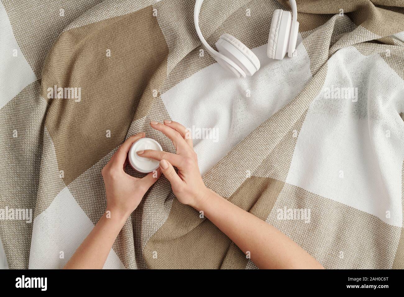 Diseño plano de manos de mujer joven tomando crema facial de jar en el Plaid Foto de stock