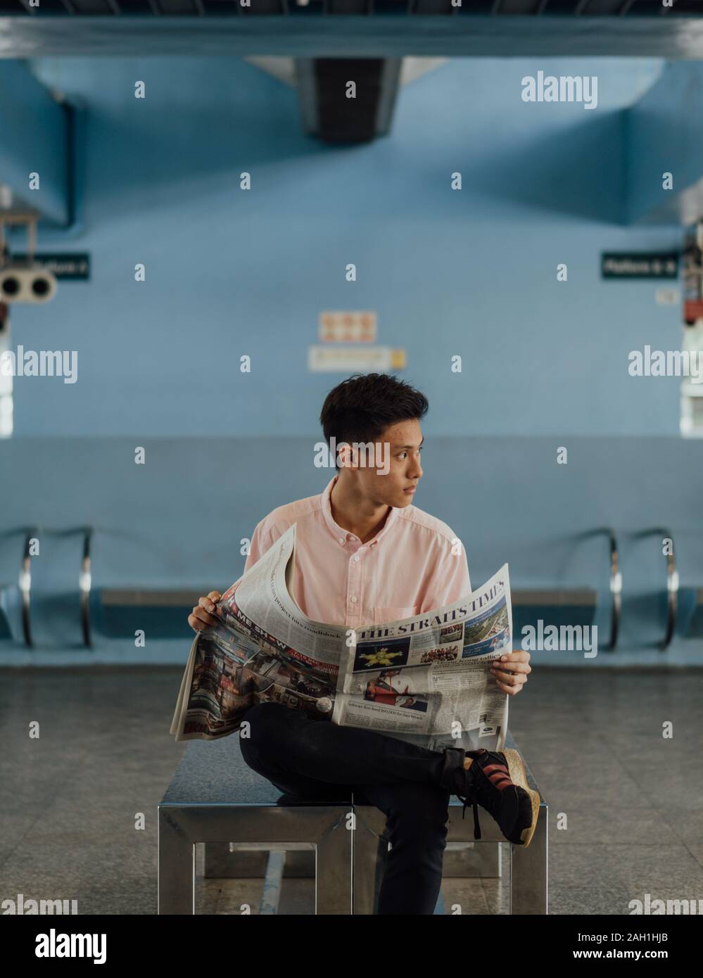 Macho de Singapur vistiendo una camiseta rosada, mientras lee el periódico Straits Times en Queenstown MRT, mirando a la derecha Foto de stock