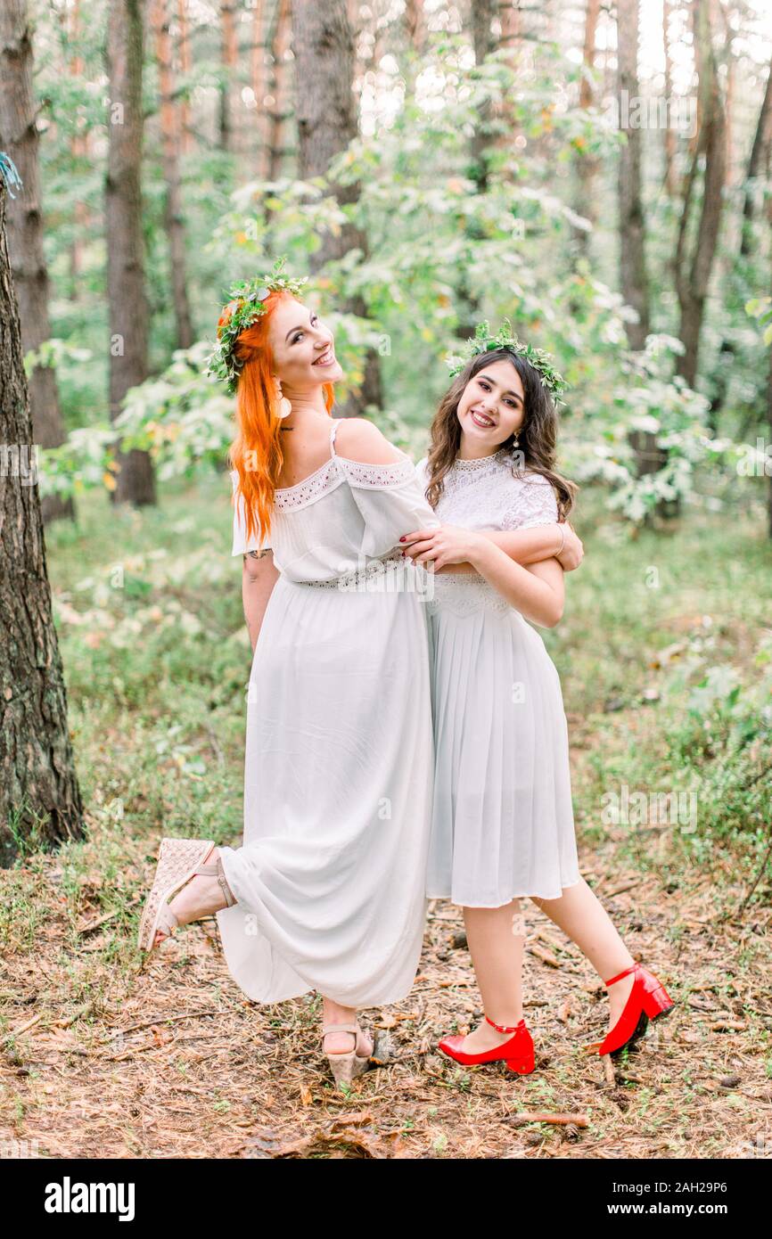 Gracioso dos chicas guapas damas de honor la danza en el bosque. Dos damas  de honor vestidos de blanco y las guirnaldas en la cabeza sonriente y  divertirse juntos Fotografía de stock -