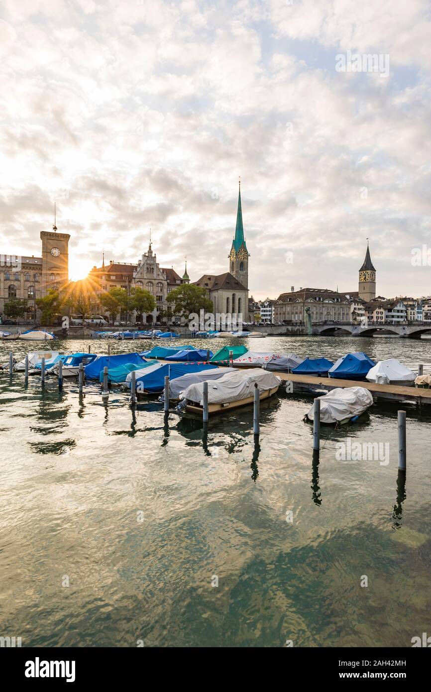 Suiza, en el cantón de Zurich, Zurich, cubiertas embarcaciones amarradas en el río Limmat al atardecer con Old Town Waterfront en segundo plano. Foto de stock