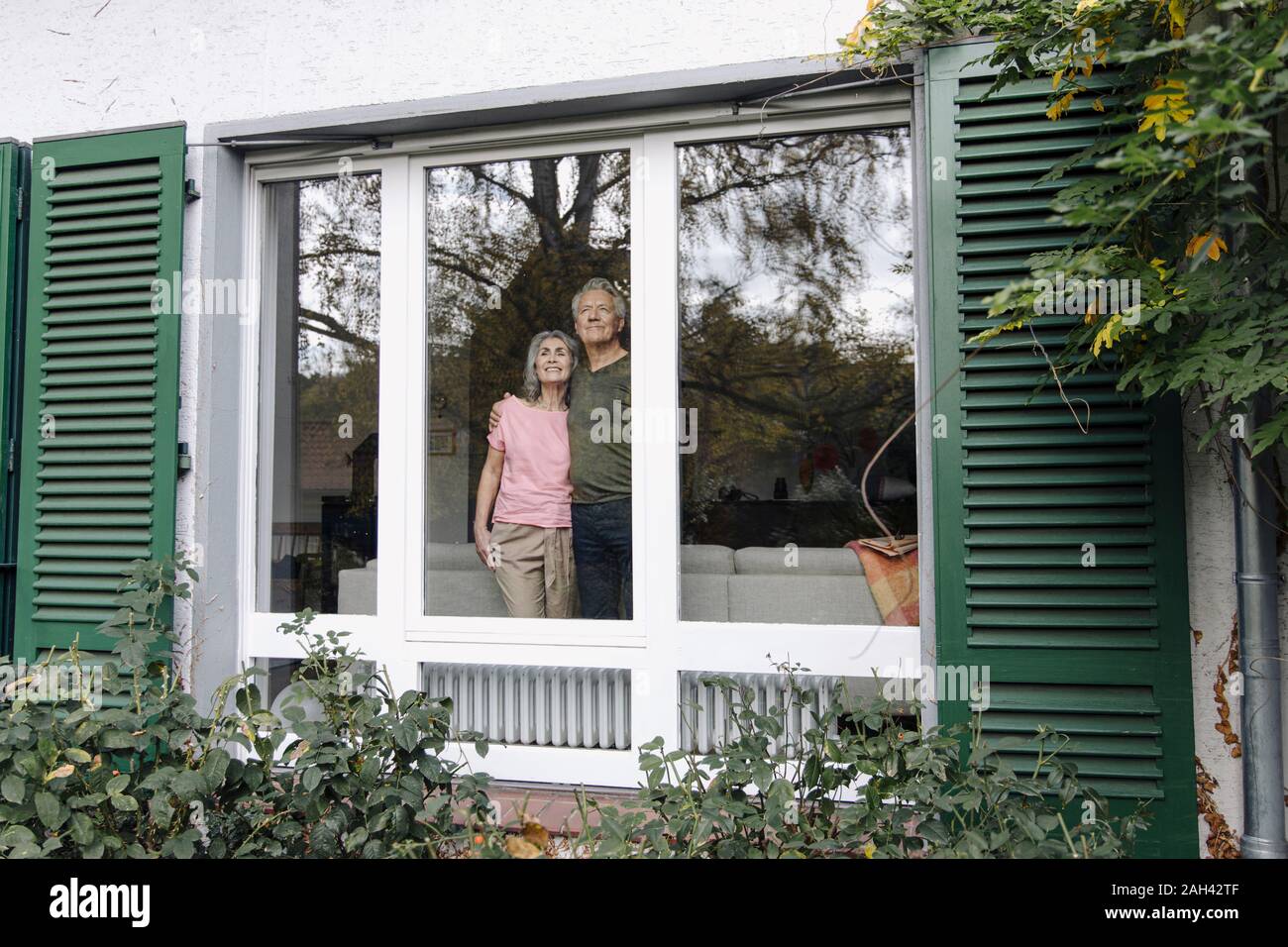 Pareja Senior detrás del cristal de su casa mirando Foto de stock